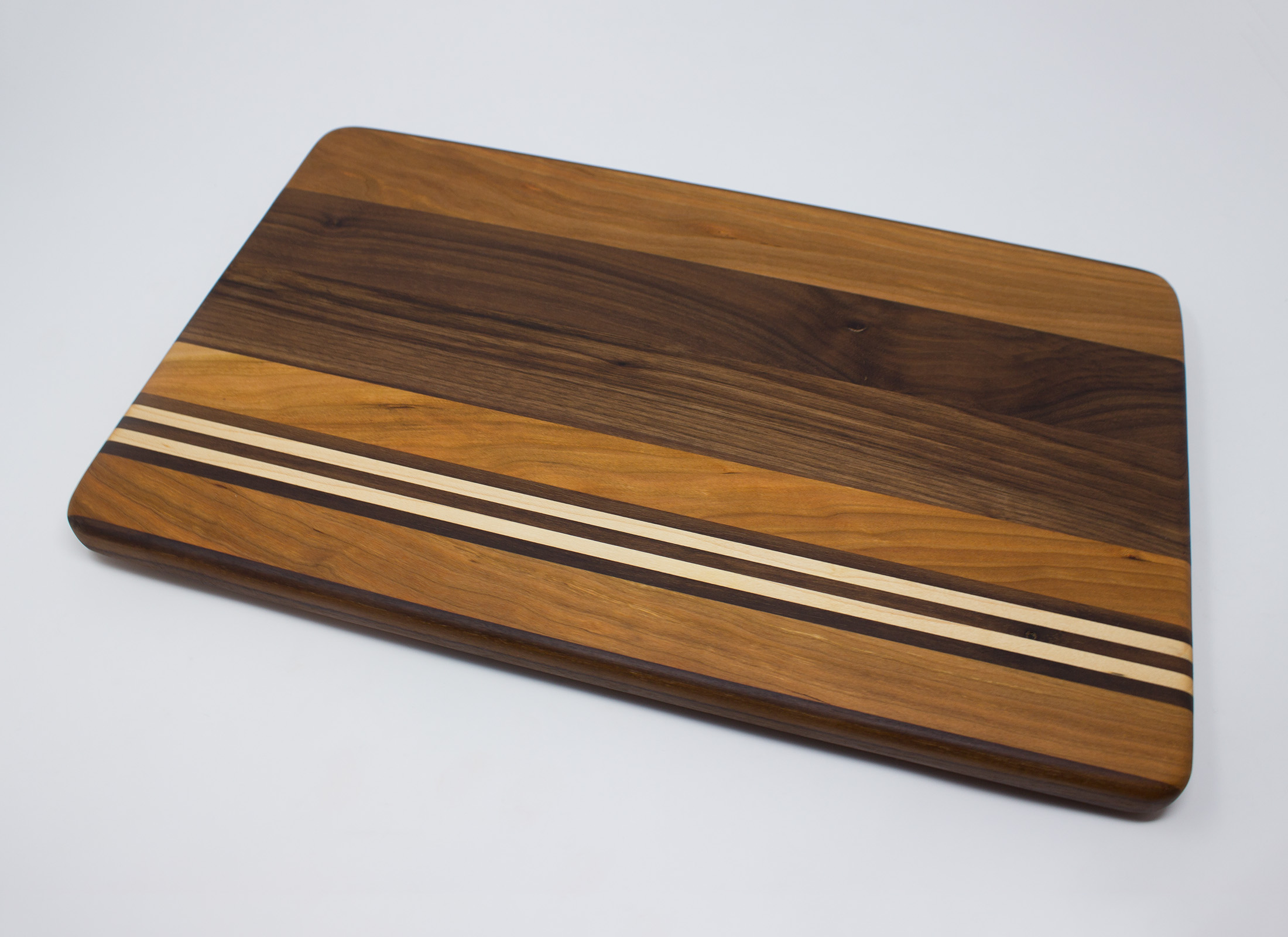 https://www.rockfordwoodcrafts.com/wp-content/uploads/Cherry-Walnut-and-Maple-with-Offset-Stripes-Cutting-Board-Top-Angled.jpg